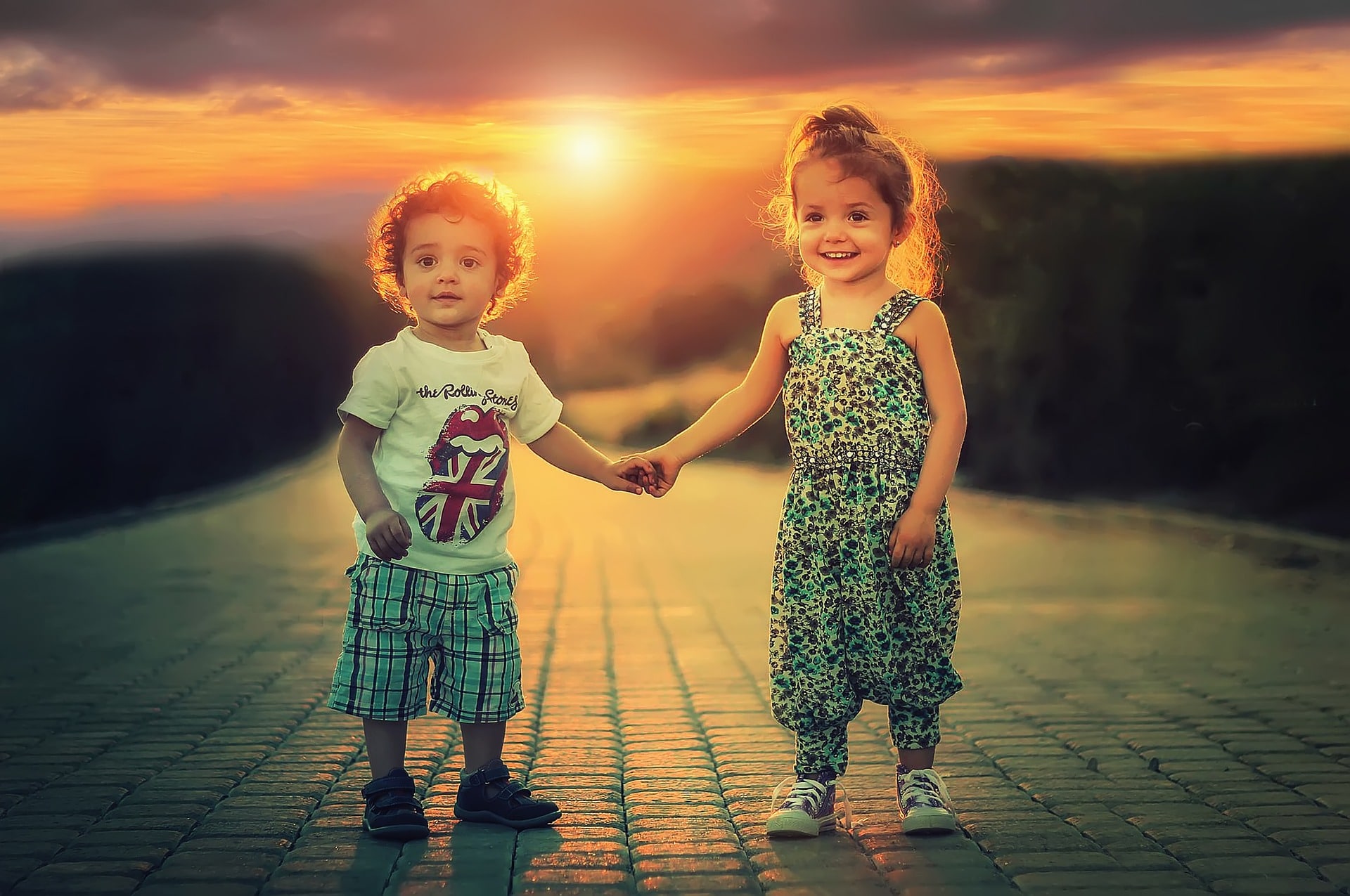 kaksi lasta pitävät toisiaan kädestä auringon laskiessa taustalla
