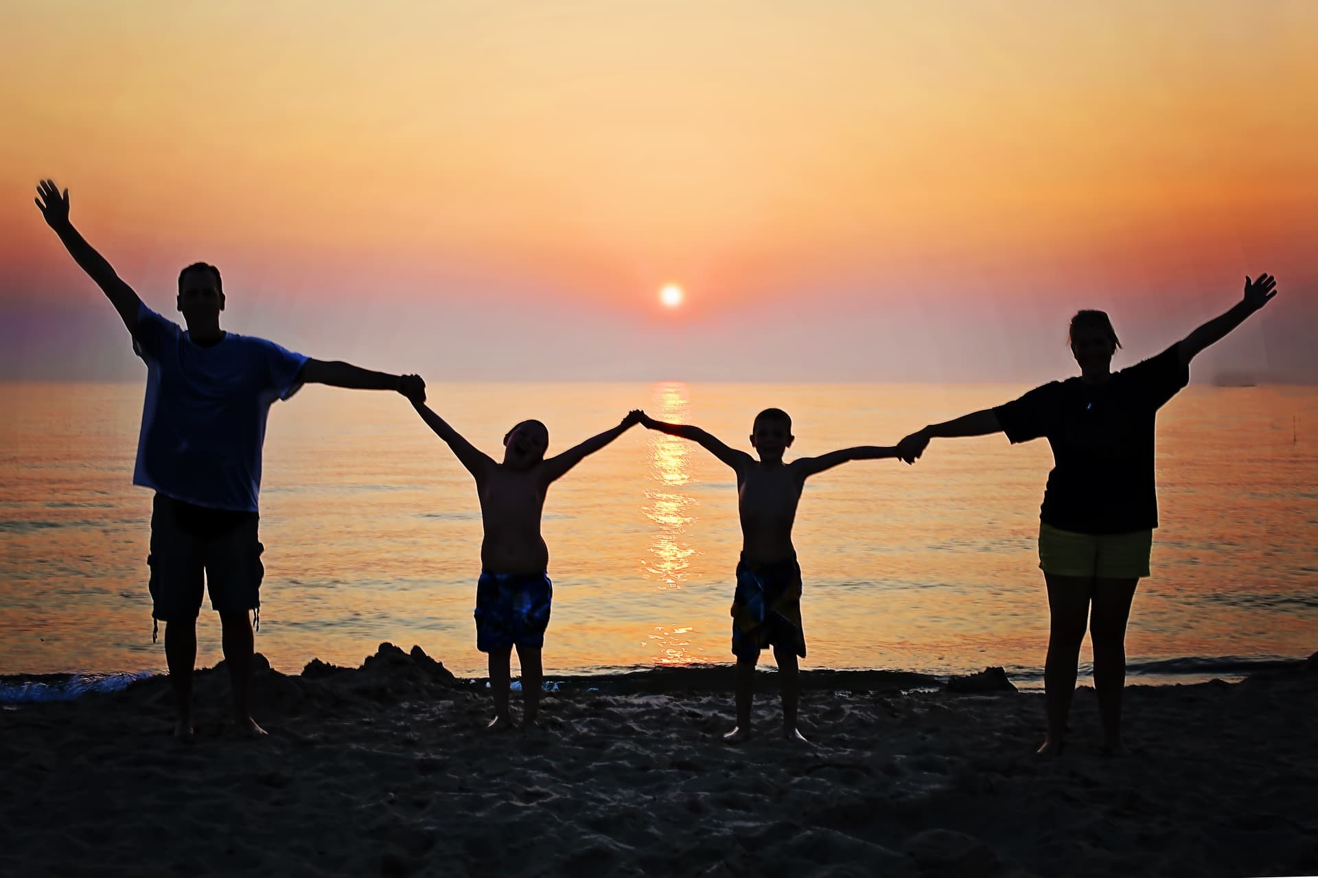 Perhe pitää toisiaan kädestä rannalla auringon laskiessa