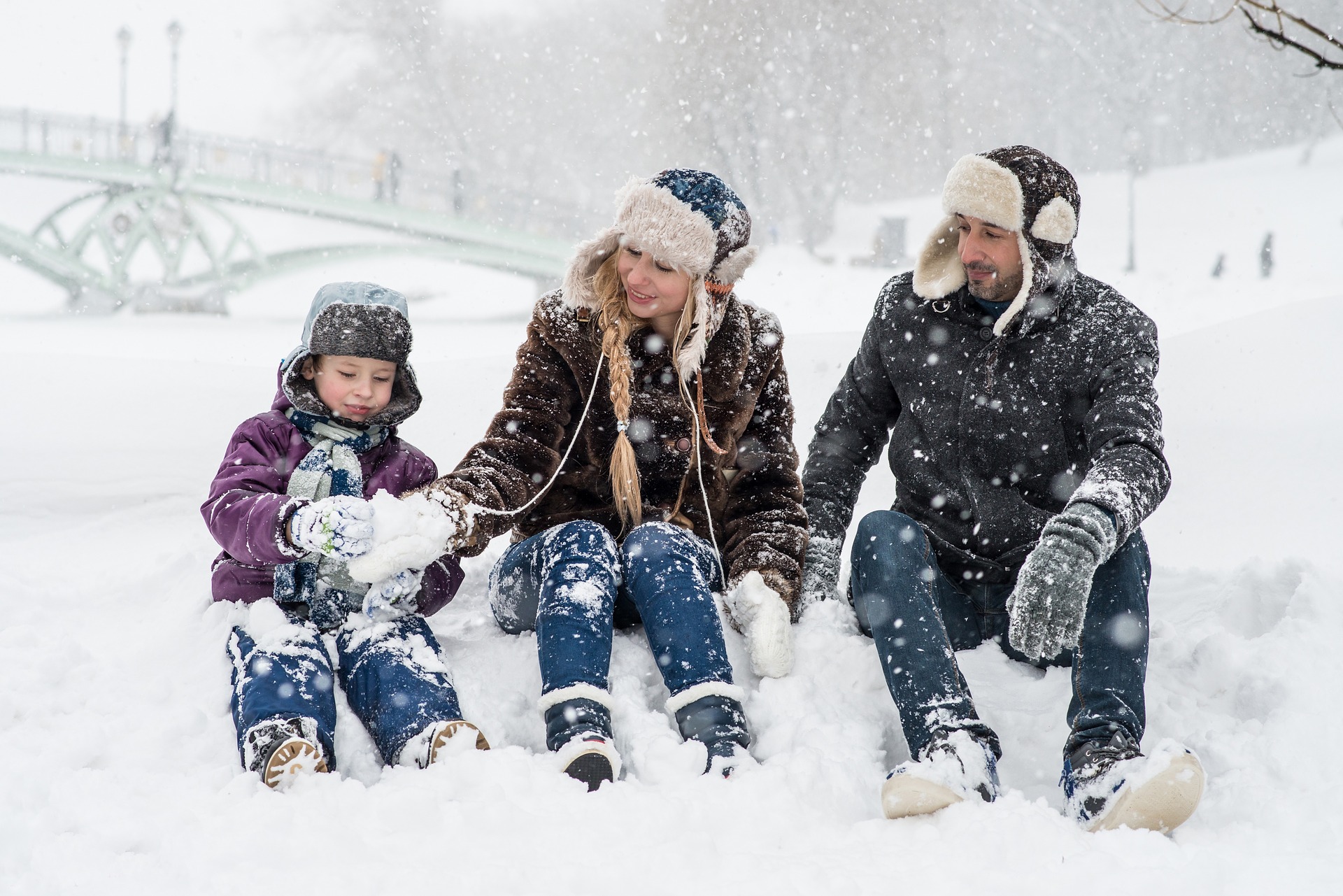 Lapsi ja vanhemmat istuvat lumihangessa